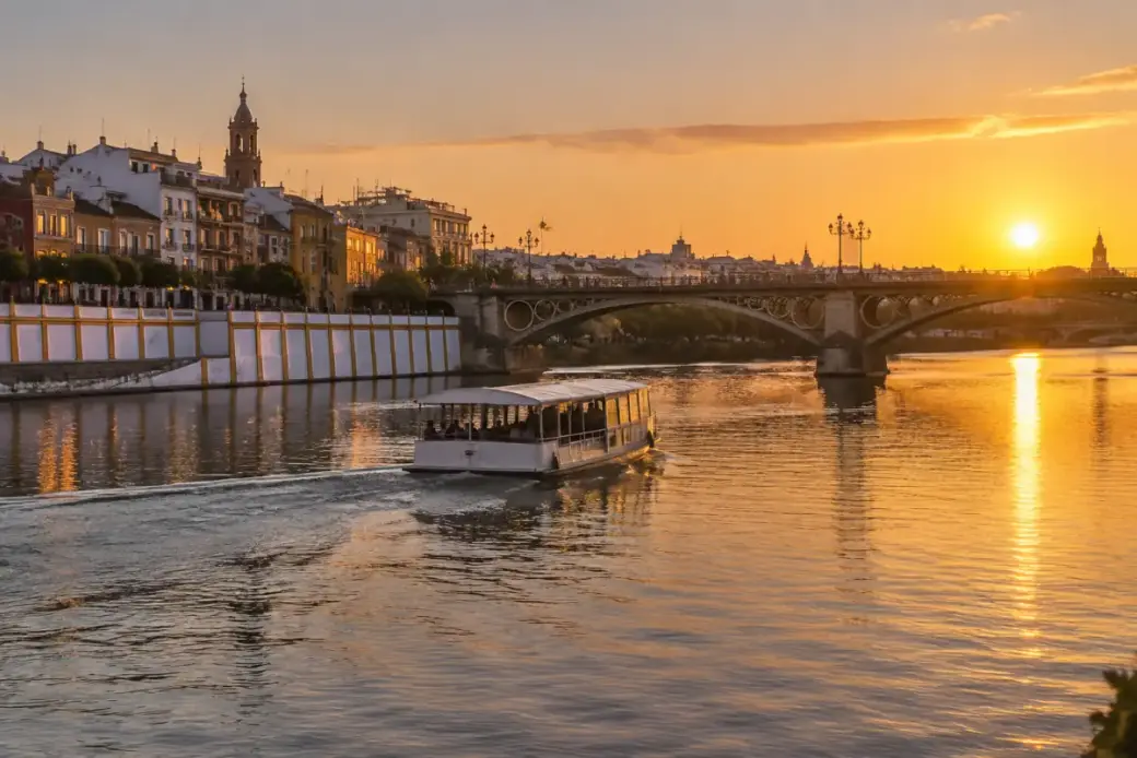 Barco turístico navegando por el Guadalquivir al atardecer junto al puente de Triana