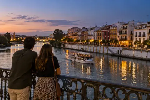 Pareja en el puente de Triana al anochecer mientras un barco pasa por el Guadalquivir