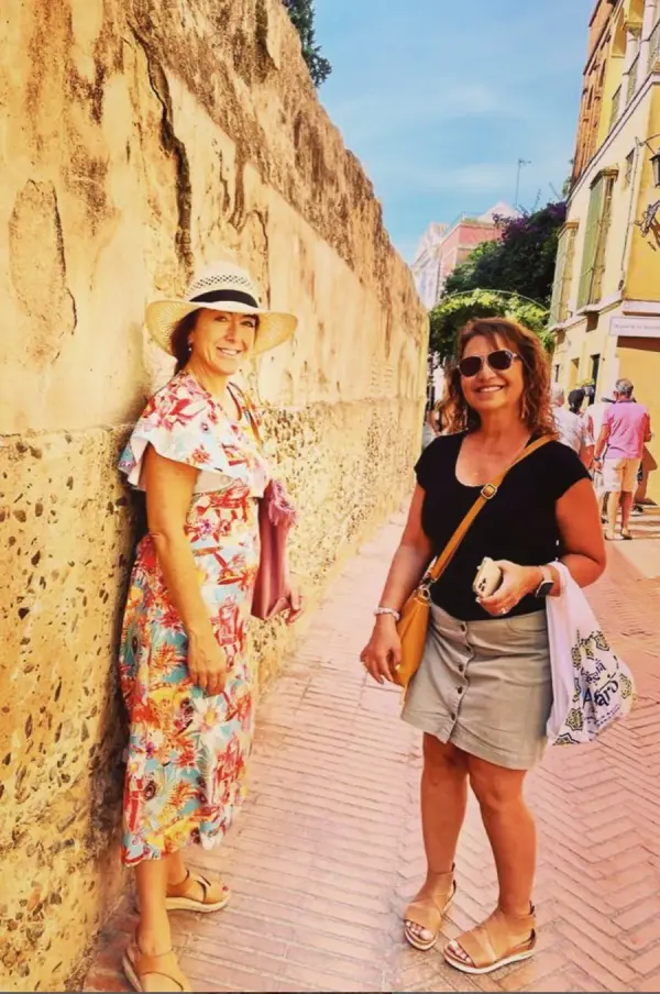 María y una viajera junto a un muro antiguo de piedra en una calle del centro de Sevilla