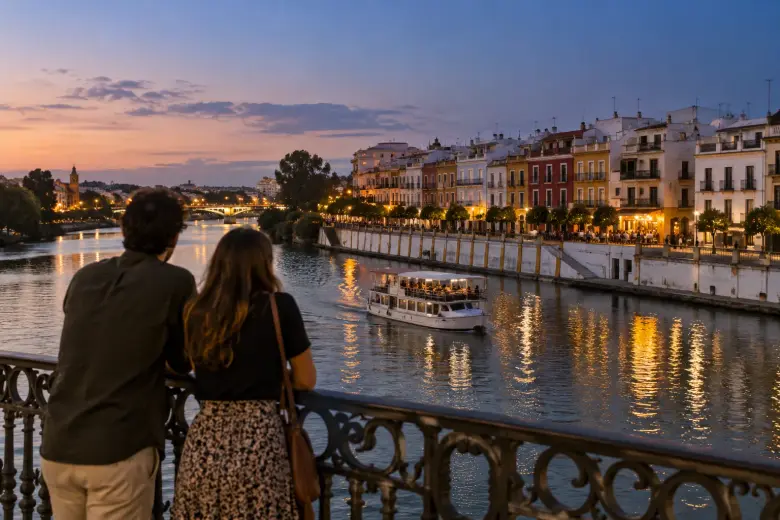 Pareja en el puente de Triana al anochecer mientras un barco turístico pasa por el Guadalquivir frente a la calle Betis