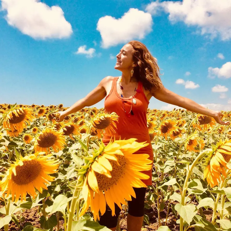 María Ramírez with open arms in a sunflower field under a blue sky